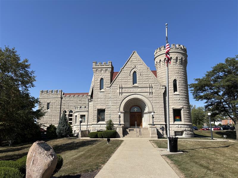 Exterior view of The Brumback Library in Van Wert, Ohio. The castle-like building is framed by trees on either side with a clear blue sky in the background. 