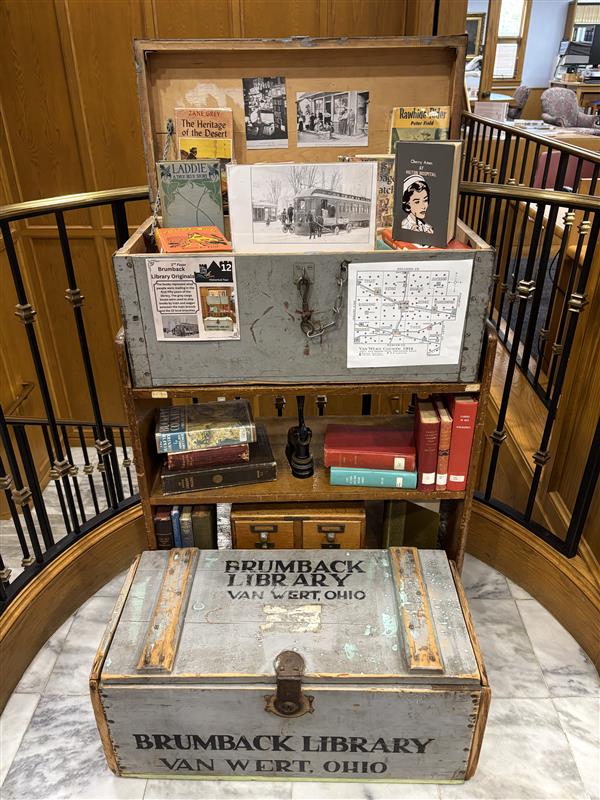 A historical display of stacked books and gray cargo trunks featured on the library's self-guided tour. The cargo boxes held books en route between the main library and local branches by train and wagon. 