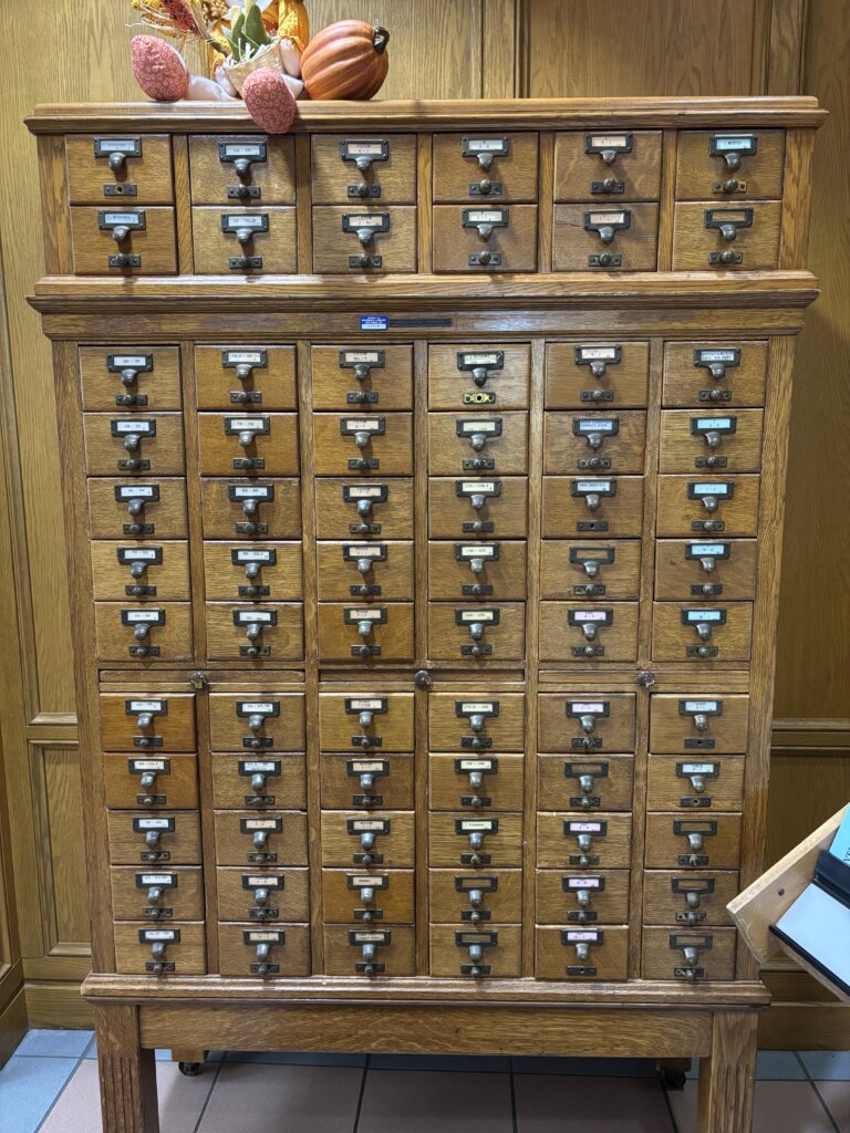 An image of an old, wood card catalog topped with seasonal autumnal decor at The Brumback Library